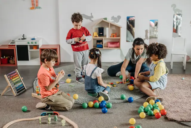 Crianças brincando com bolinhas coloridas e uma educadora